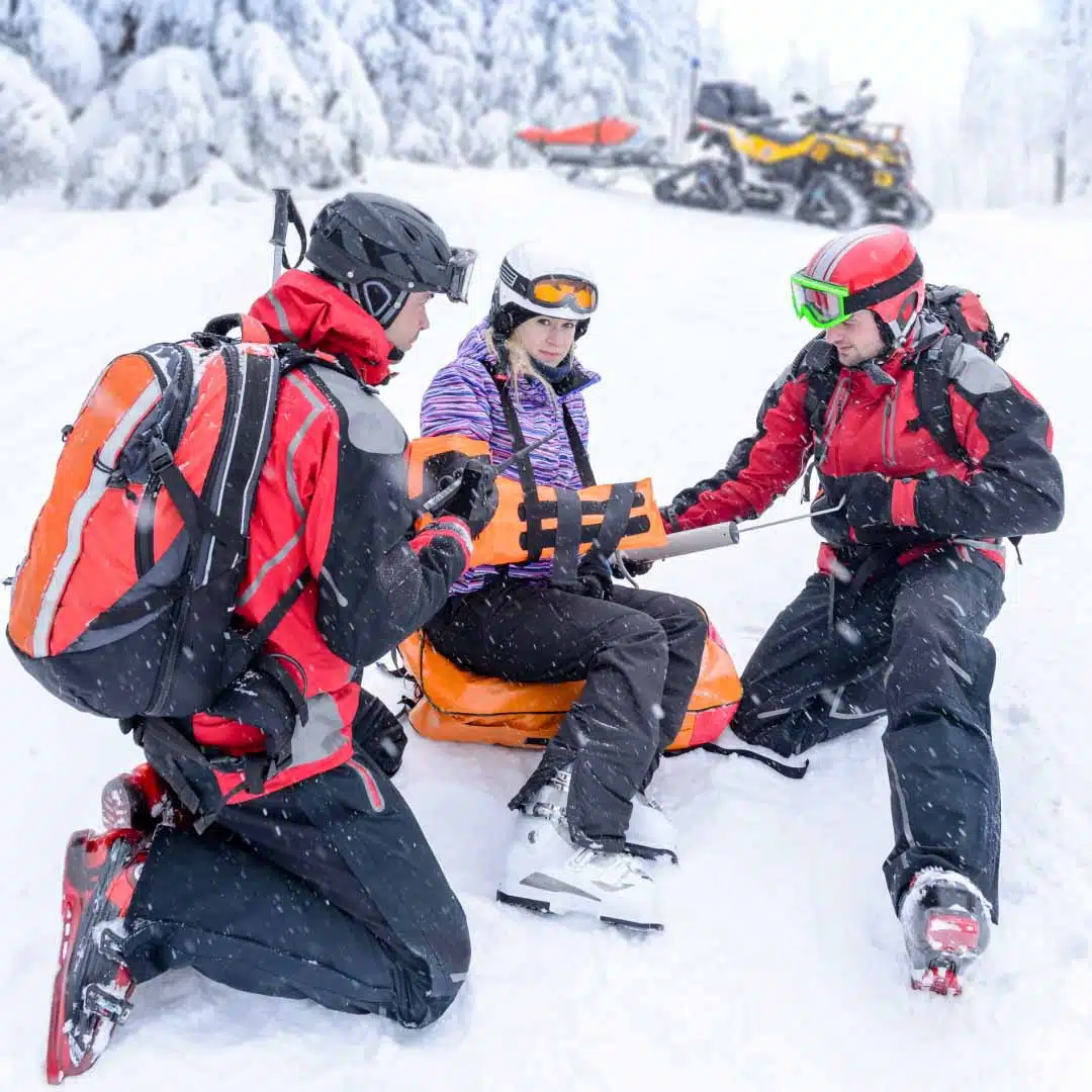 femme entourée de 2 sauveteurs suite à un accident de ski